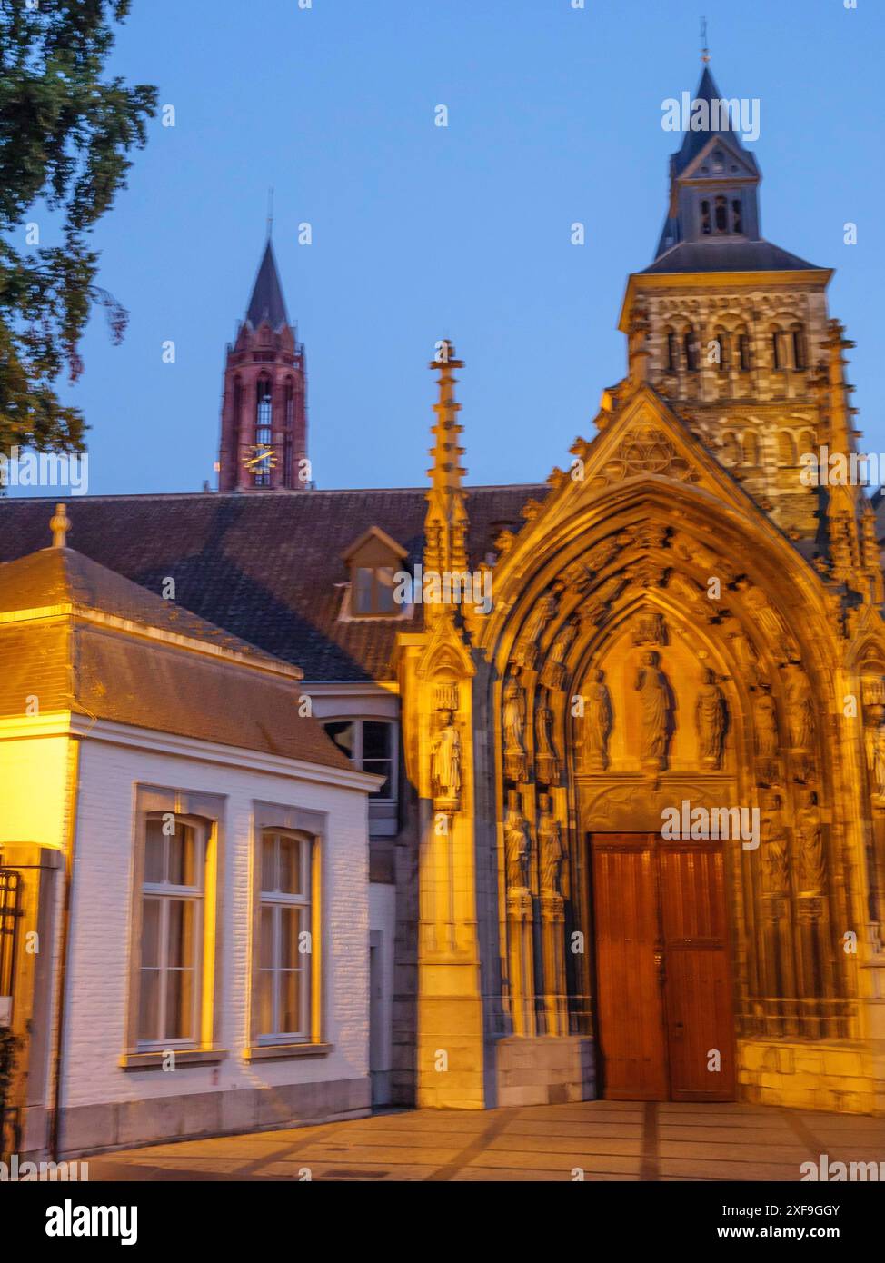 Kirchengebäude mit einem reich verzierten gotischen Portal und einem beleuchteten Kirchturm in der Abenddämmerung, maastricht, niederlande Stockfoto