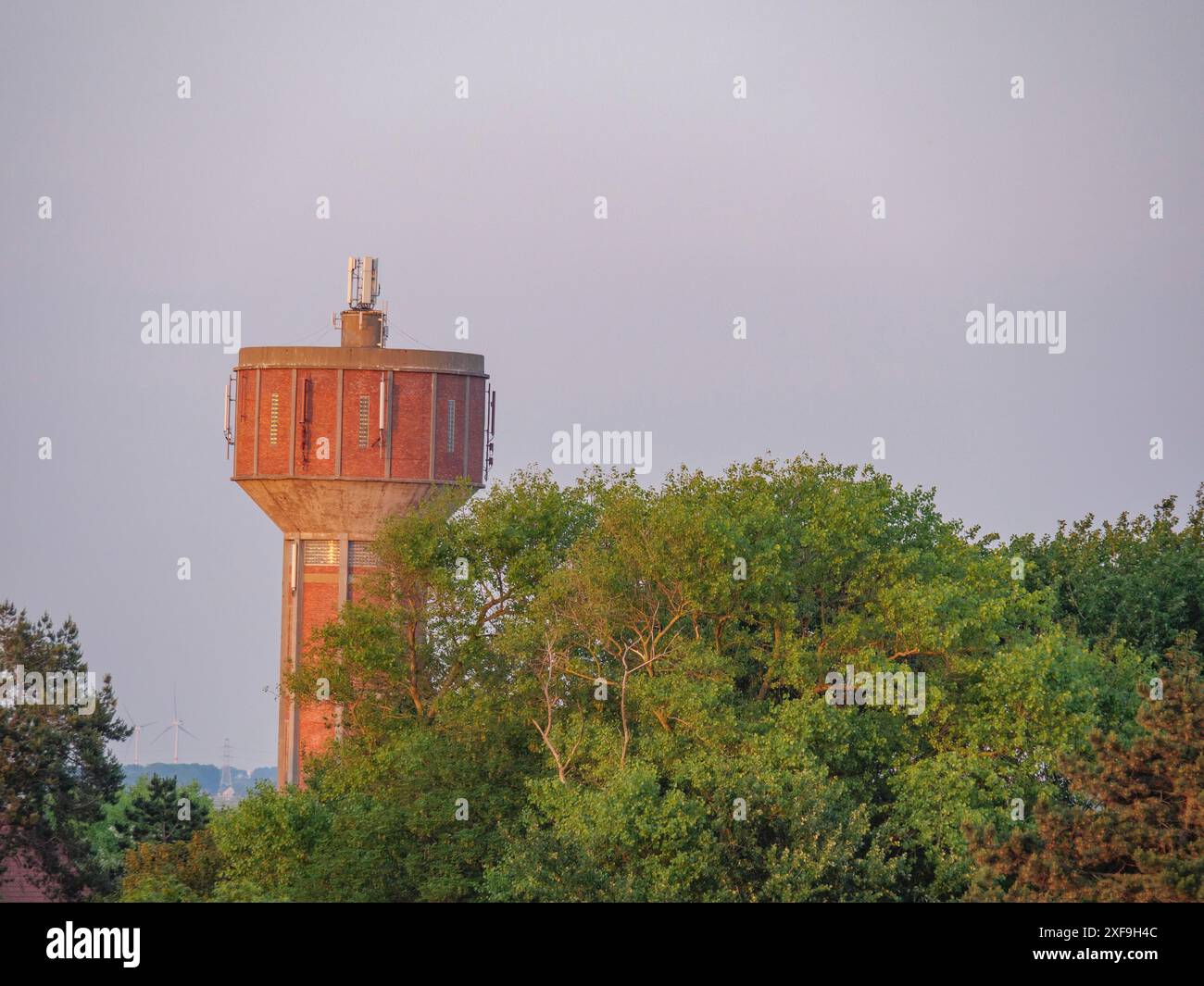 Roter Wasserturm zwischen grünen Bäumen in der Abenddämmerung, ein Highlight architektonischer Einfachheit, oostende, belgien Stockfoto