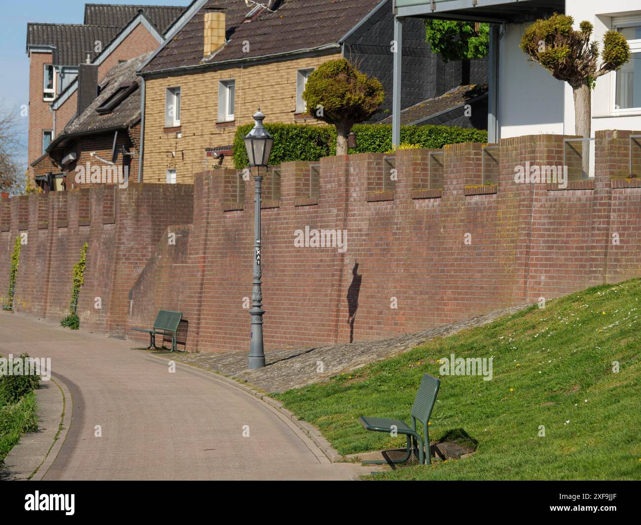 Ein ruhiger Weg mit Bänken führt entlang einer hohen Backsteinmauer und den Fassaden von Häusern, beleuchtet von Straßenlaternen, rees, niederrhein, deutschland Stockfoto