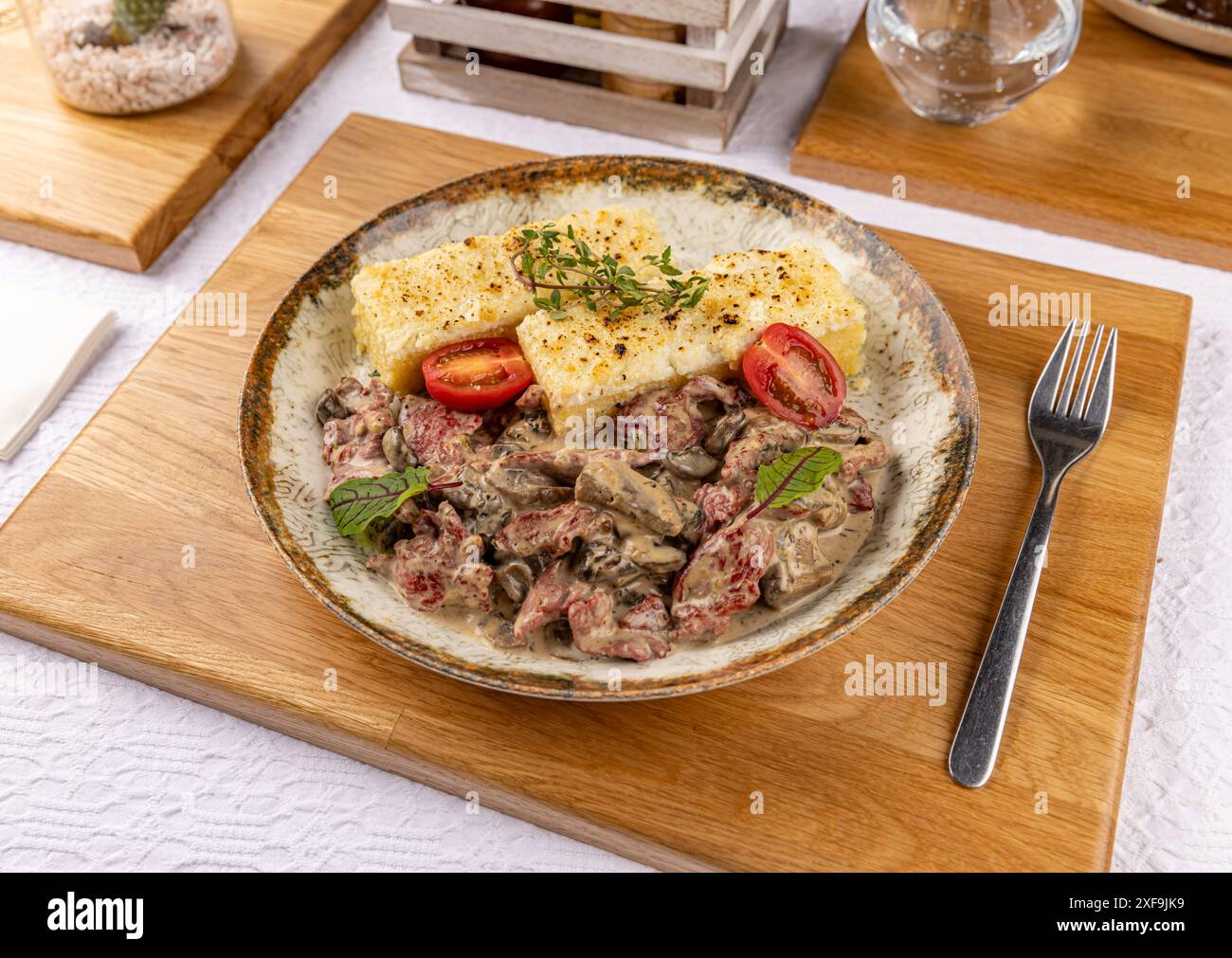 Rinderstroganoff mit cremiger Pilzsauce und gebackener Polenta, serviert auf einem Teller auf einem Restauranttisch Stockfoto