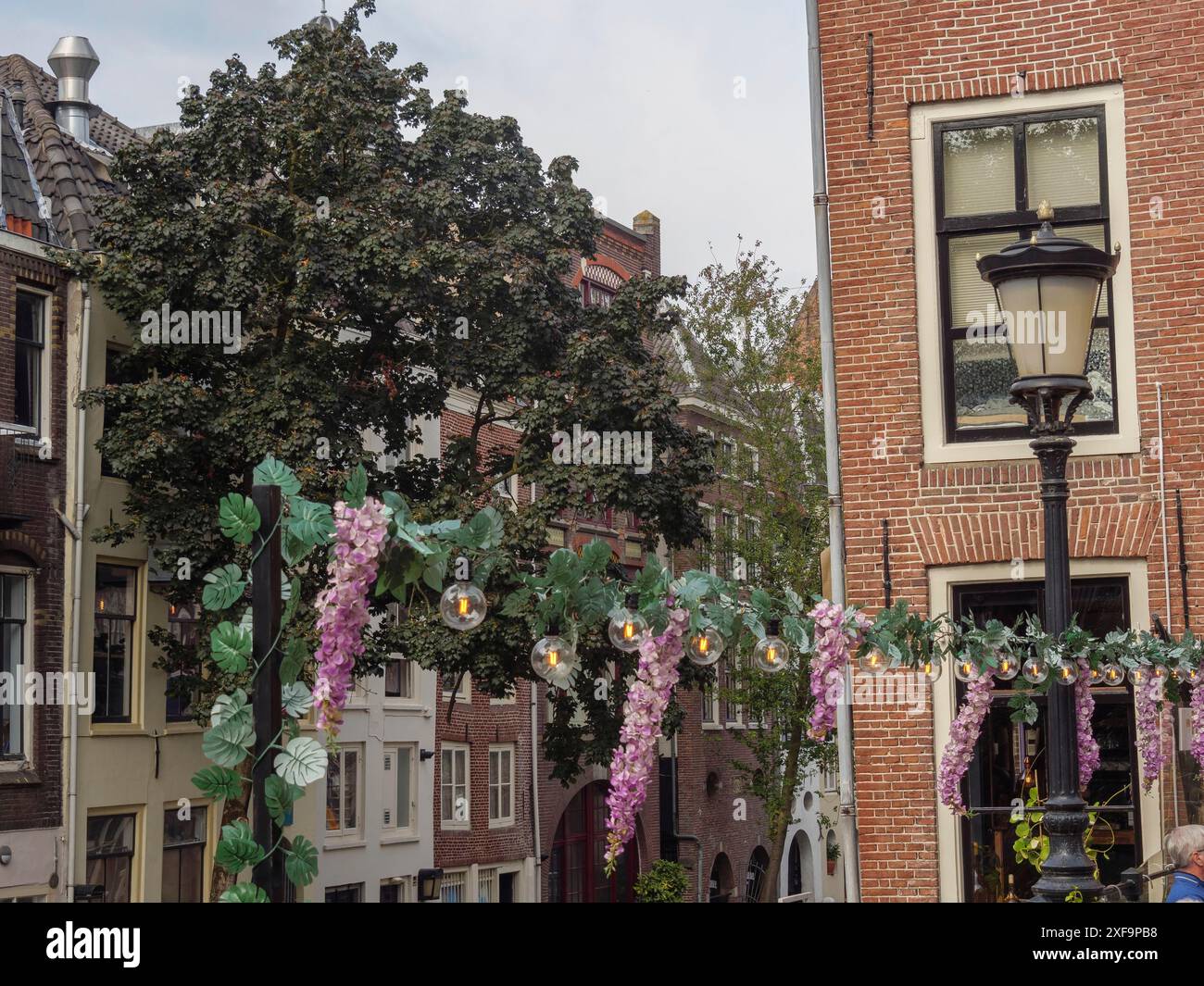Mit Blumen und Feenlichtern geschmückte Laternenpfahl vor historischen Gebäuden und einem Baum, utrecht, niederlande Stockfoto