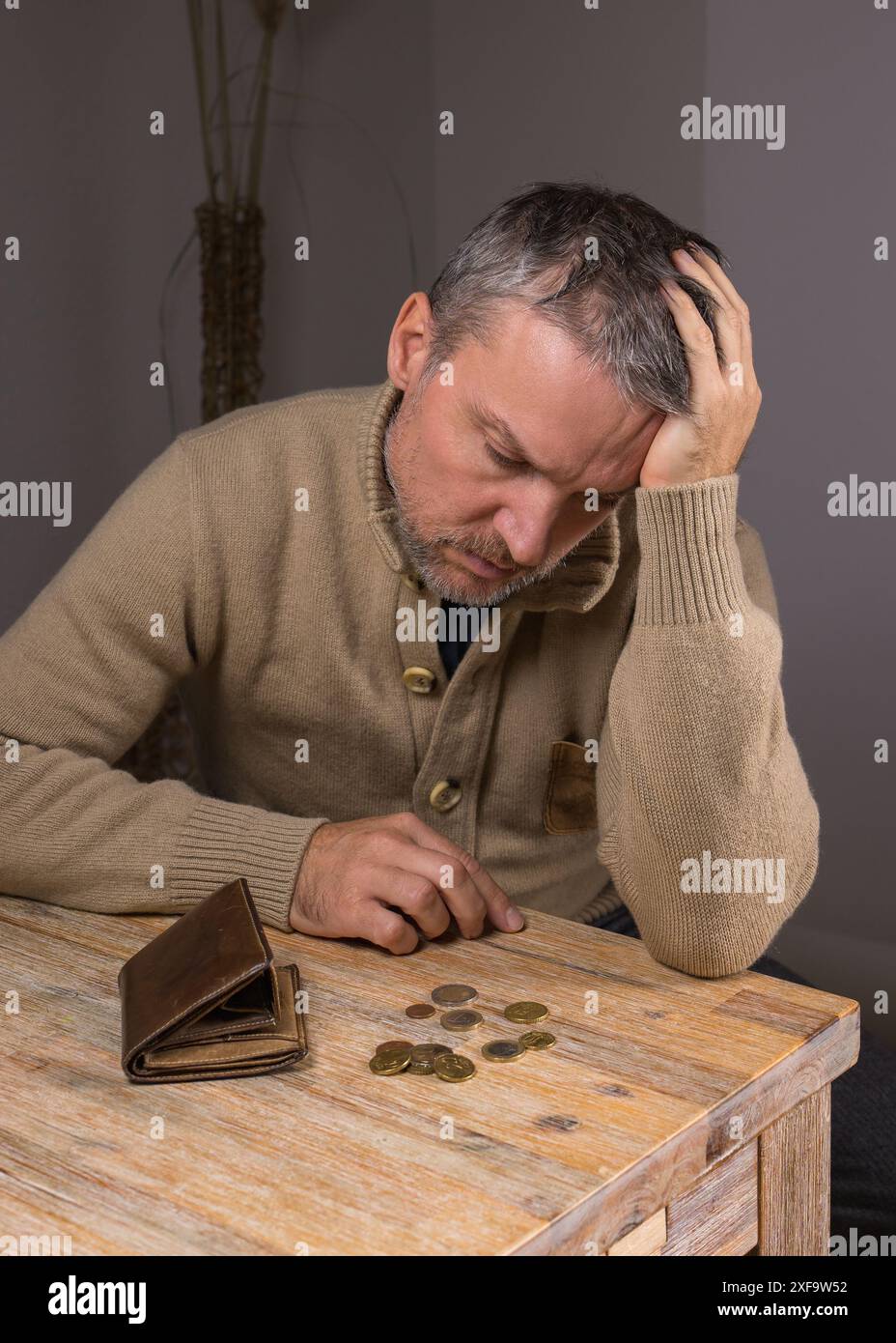 Ein Mann mit Bart untersucht kleine Geldwechsel. Ein armer Mann mittleren Alters sitzt zu Hause, vor ihm liegt eine leere Geldbörse und die letzten Metallmünzen, Geld. E Stockfoto
