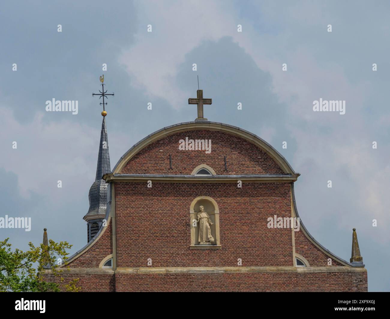 Nahaufnahme der Kirchenfassade mit Kreuz, Statue und Turm unter bewölktem Himmel, Vreden, Nordrhein-Westfalen, Deutschland Stockfoto