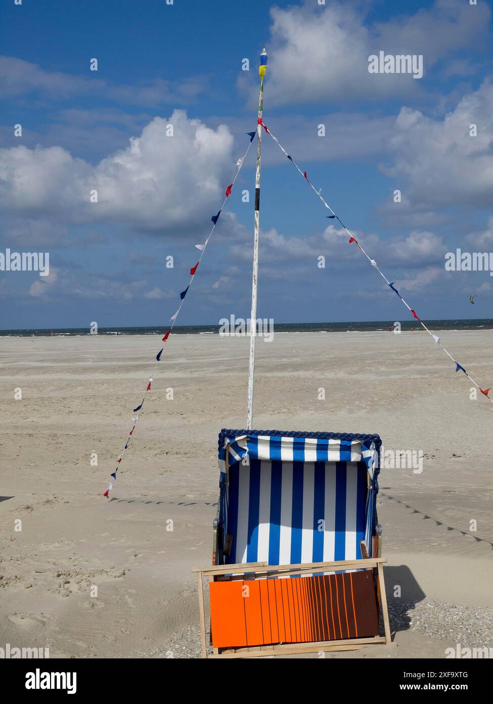 Einfach gestreifter Strandstuhl mit Fahnen, breiter Sandstrand, Himmel mit Wolken, Juist, Ostfriesland, Deutschland Stockfoto