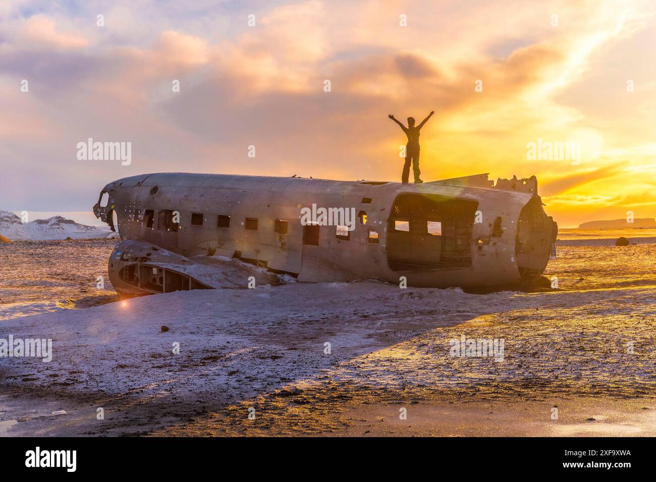 Frau auf dem Rücken mit den Armen oben auf dem Solheimasandur-Flugzeug bei einem Wintersonnenaufgang in Island Stockfoto