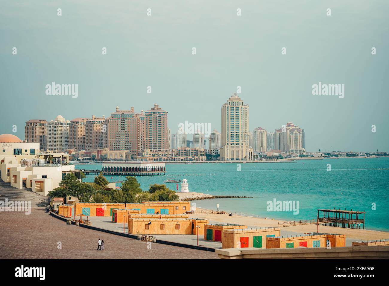 Panoramablick auf moderne Hochhäuser entlang der Uferpromenade in Doha, Katar, mit klarem Himmel und türkisfarbenem Wasser Stockfoto