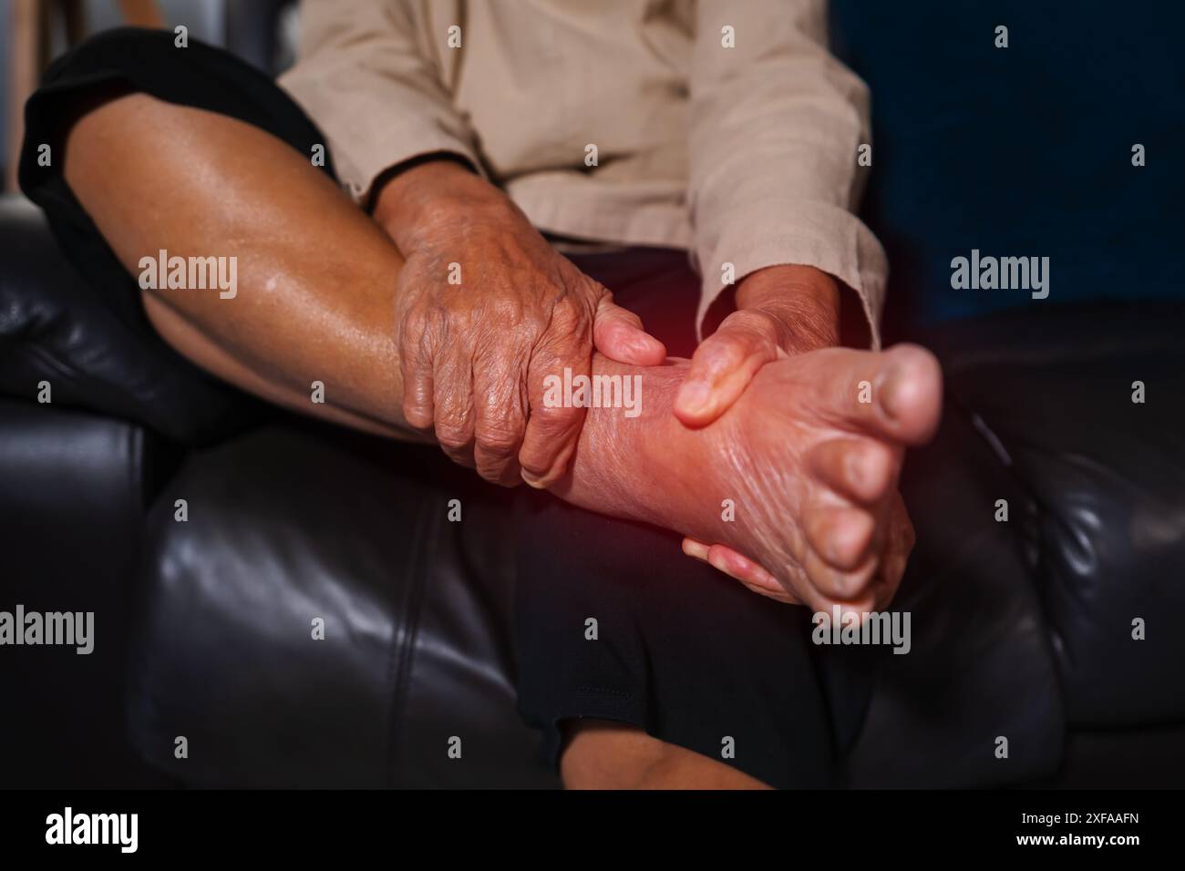Schließen Sie eine ältere Frau an, die an Fuß- und Knöchelschmerzen leidet, während sie nachts auf einem Sofa im Wohnzimmer sitzt Stockfoto