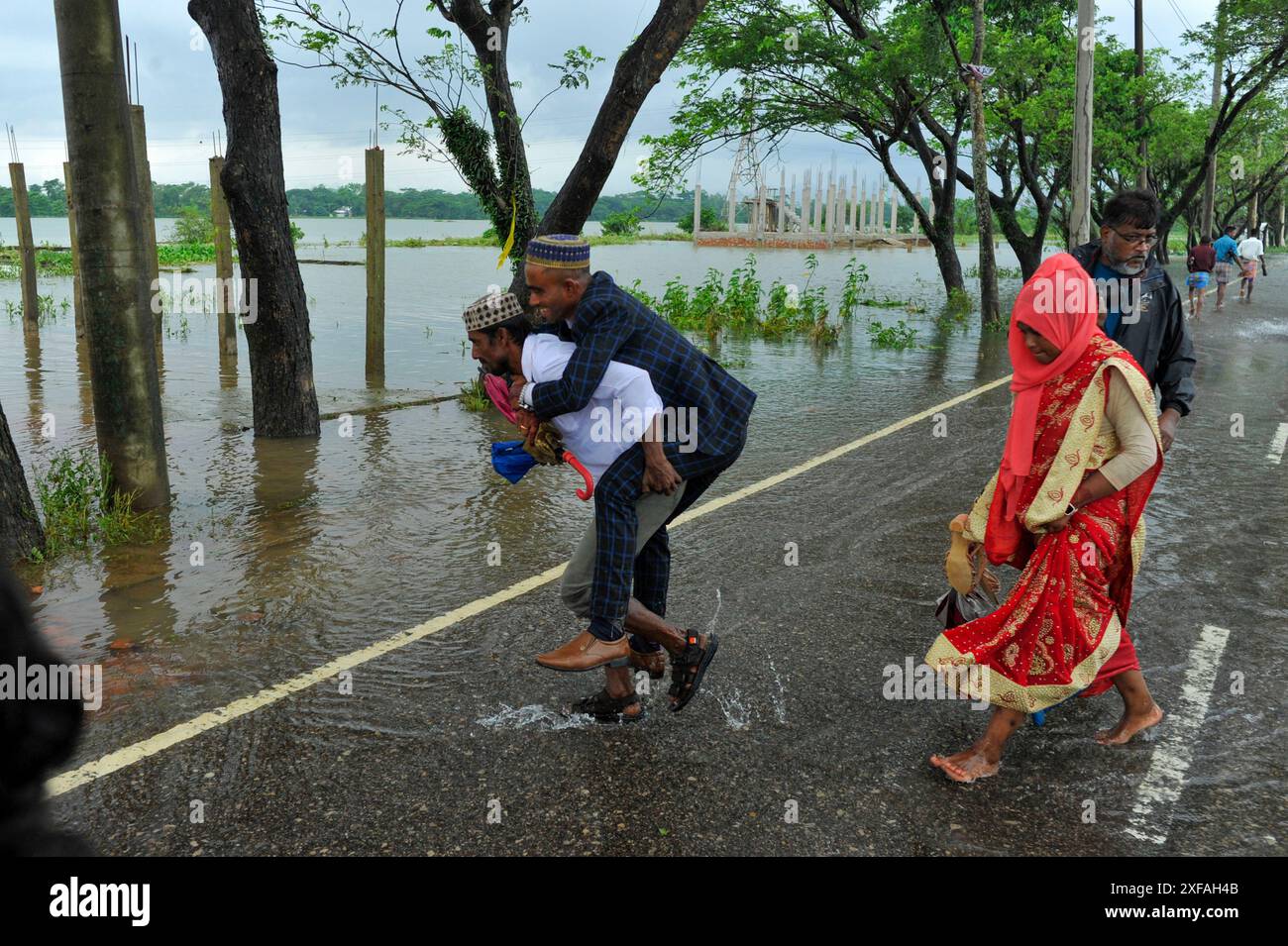 Ein Verwandter trägt einen frisch verheirateten Bräutigam auf dem Rücken, um die überflutete Chatak-Gobindganj-Straße im Sunamganj-Bezirk von Sylhet, Bangladesch, zu überqueren. Stockfoto