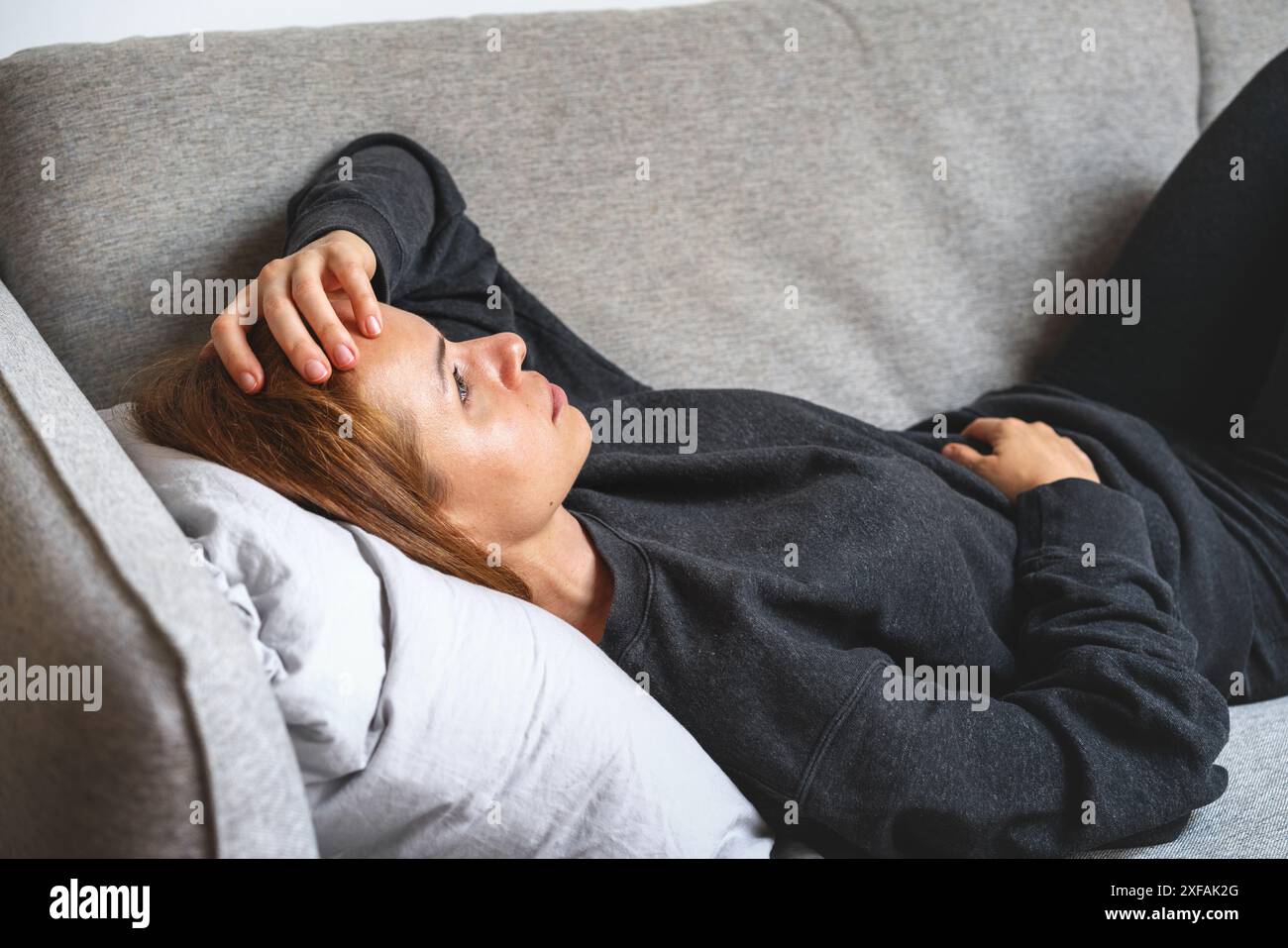 Junge Brünette, die auf dem Sofa liegt und den Kopf mit der Hand hält. Depression, Überarbeit, Geisteskrankheiten. Stockfoto