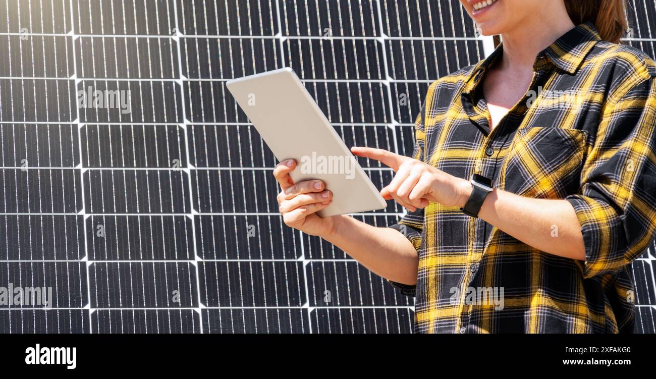 Eine Ingenieurin arbeitet an einem digitalen Tablet vor einem Sonnenkollektor in einem Solarkraftwerk. Stockfoto