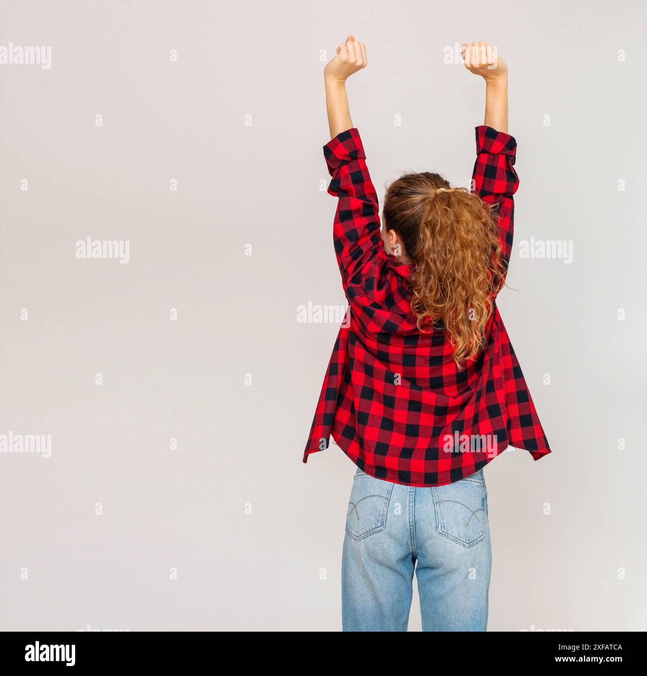 Rückansicht einer lässigen tragenden Frau, die die Arme nach oben streckt. Stockfoto