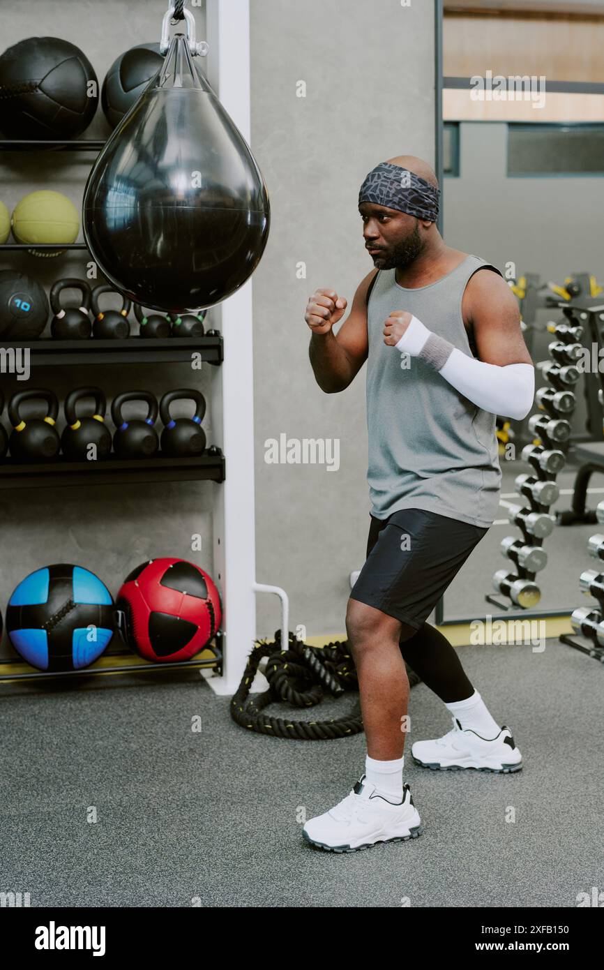 Junger afroamerikanischer Mann, der vor dem Training einen schwarzen Ledersack boxt Stockfoto
