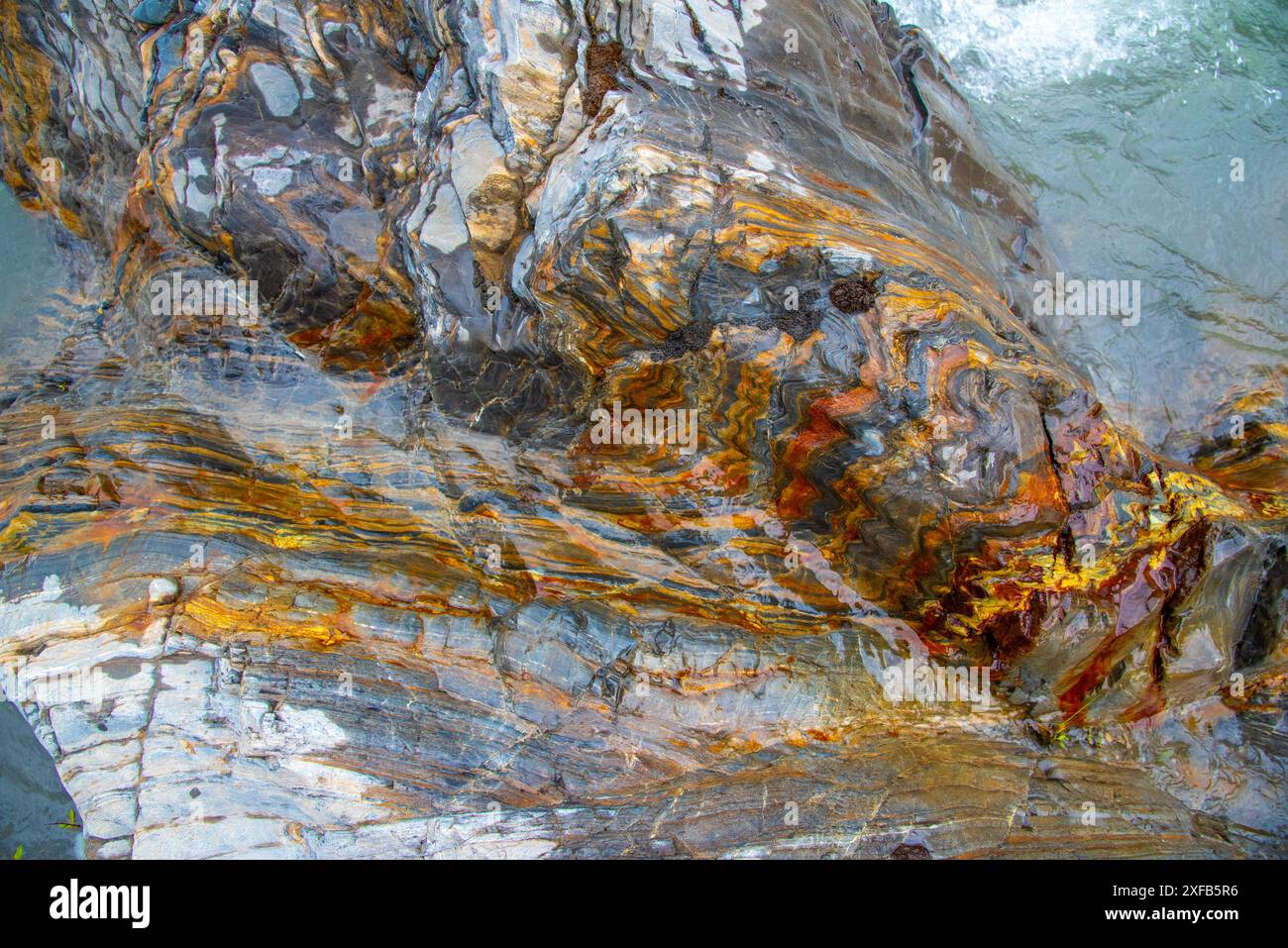 Atemberaubende farbenfrohe Felsen, die im Norden Kanadas zu sehen sind, mit nassem, feuchtem Aussehen von einem Wildnisfluss im Yukon-Territorium. Naturhintergrund, Geogolie. Stockfoto