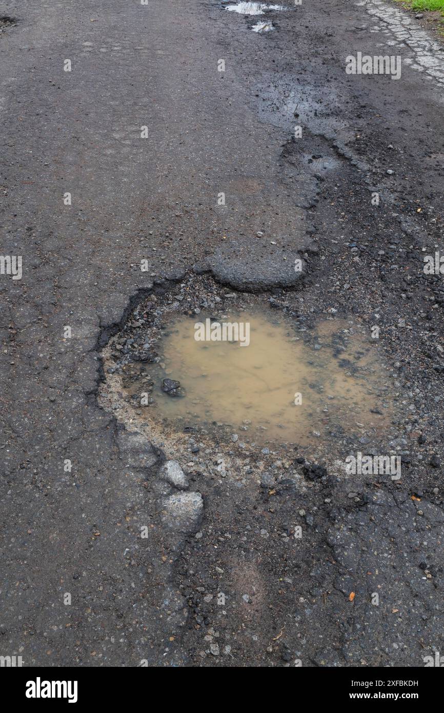 Schlagloch gefüllt mit Regenwasser auf nasser schwarzer Asphaltoberfläche im Frühjahr, Montreal, Quebec, Kanada Stockfoto