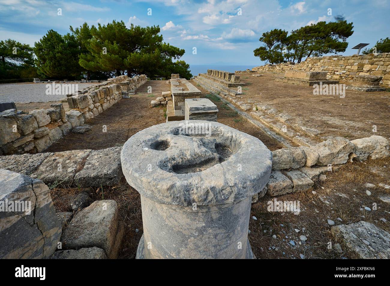 Alte Steinsäule mit erodierten Details, umgeben von Ruinen und Bäumen, Exedra, Kamiros, archäologische Stätte, antike Stadt, Gründung von Doric Stockfoto