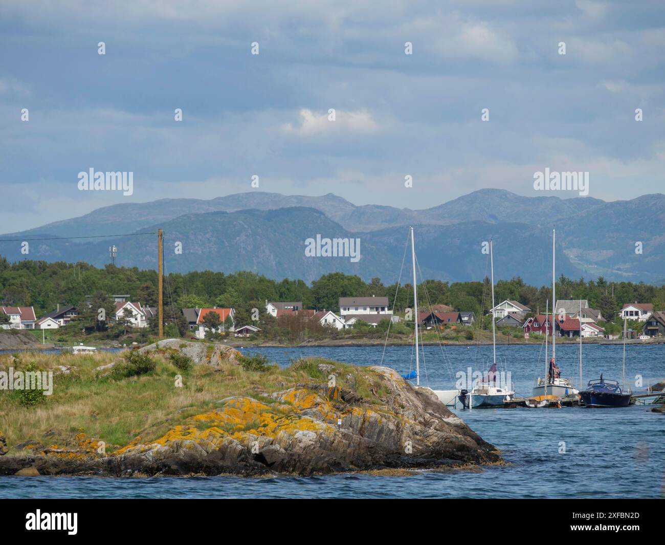 Kleine Boote, die im Wasser vor einer Küstenlandschaft aus Häusern und Bergen unter einem leicht bewölkten Himmel ankern, stavanger, norwegen Stockfoto