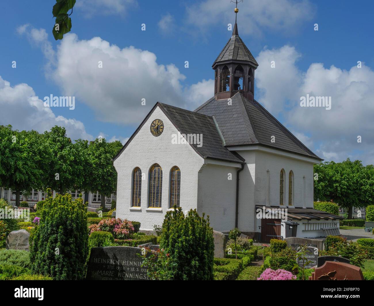 Kleine Kirche mit dunklem Dach und Turm, umgeben von bunten Blumen und Bäumen, Stein, schleswig. deutschland Stockfoto