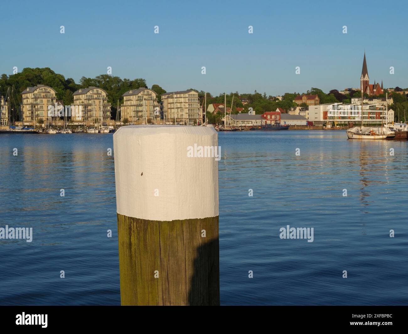 Ruhiges Hafengebiet mit einem Pfosten im Vordergrund und Kirche und Booten im Hintergrund, flensburg, schleswig-holstein, deutschland Stockfoto