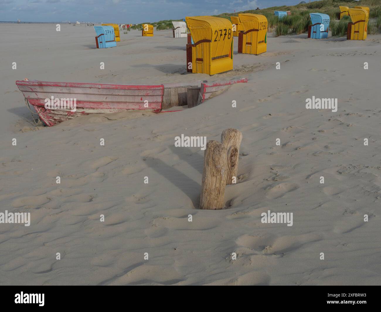 Ein altes, teilweise begrabenes Boot an einem sonnigen Strand mit Liegestühlen und leicht bewölktem Himmel, saftig, Nordsee, deutschland Stockfoto