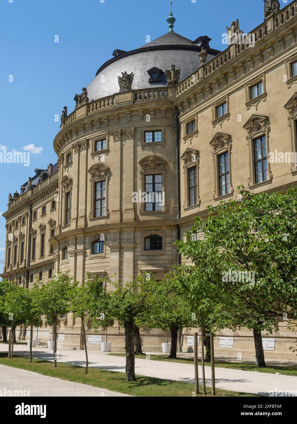 Monumentales Barockgebäude mit eleganter Fassade und kleinen grünen Bäumen im Vordergrund unter klarem blauem Himmel, würzburg, bayern, deutschland Stockfoto