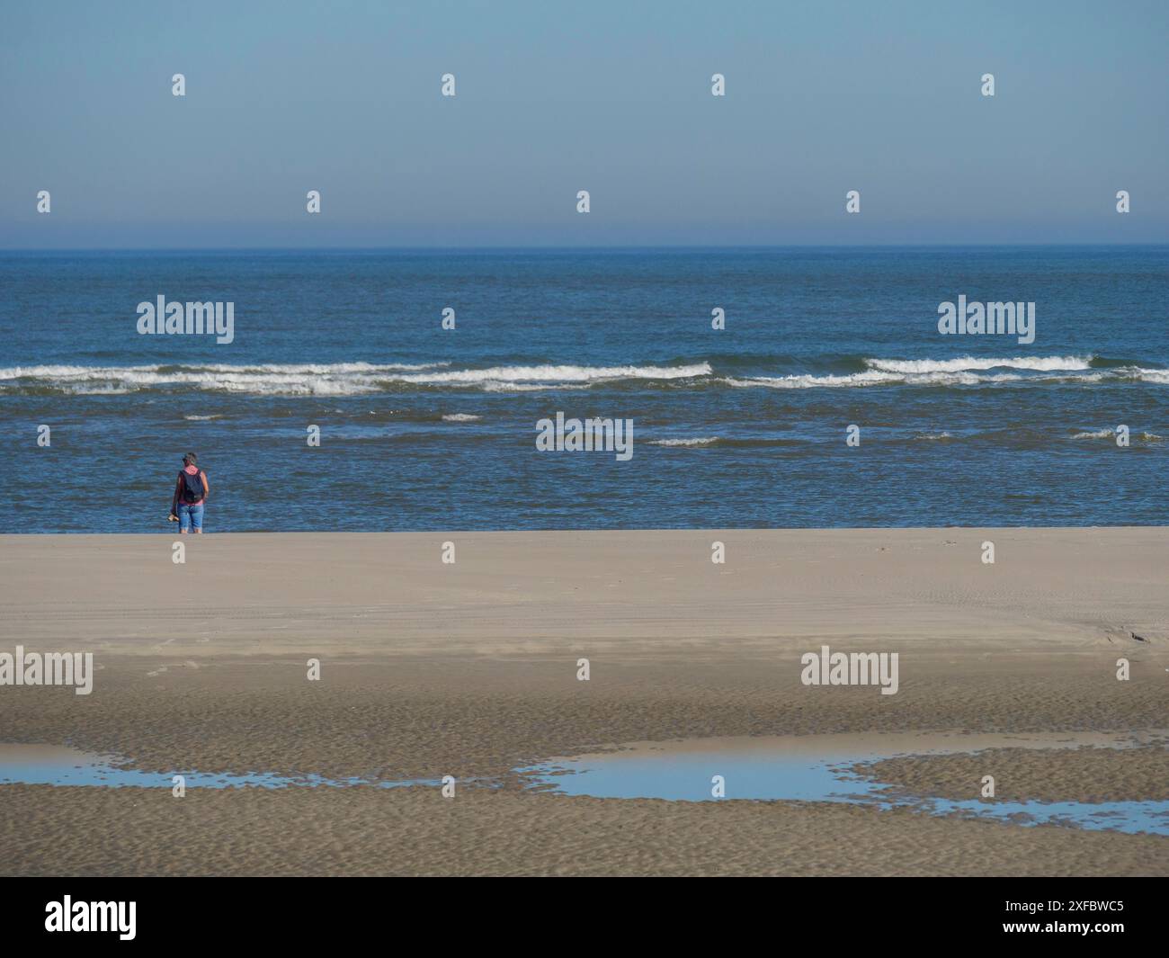 Ein Mann läuft am Ufer entlang, während die Wellen am Strand abstürzen Stockfoto