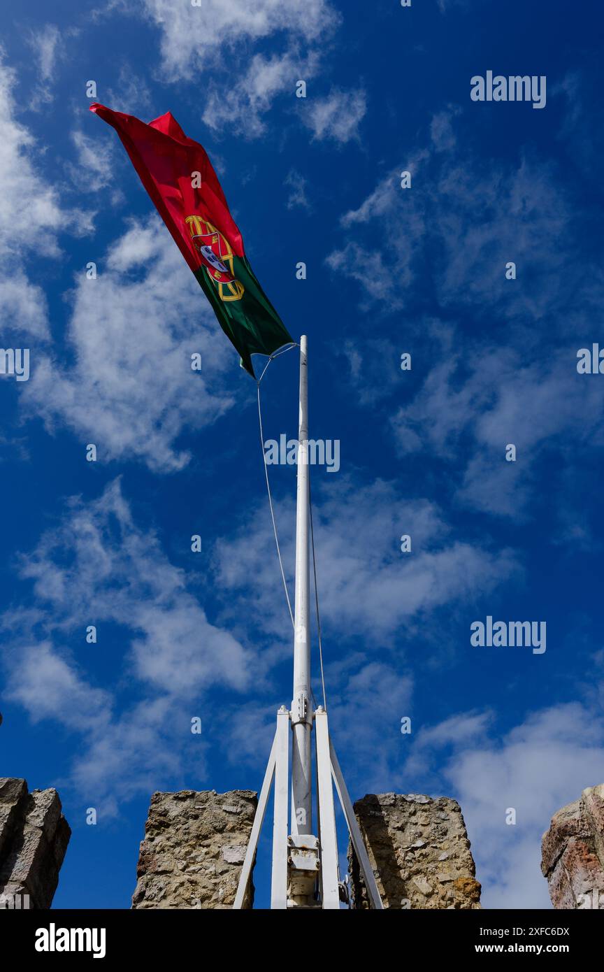 Die portugiesische Flagge fliegt hoch über den Steinmauern des Castelo de São Jorge, der vor einem leuchtend blauen Himmel steht Stockfoto