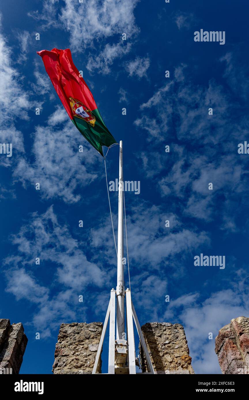 Die portugiesische Flagge fliegt hoch über den Steinmauern des Castelo de São Jorge, der vor einem leuchtend blauen Himmel steht Stockfoto