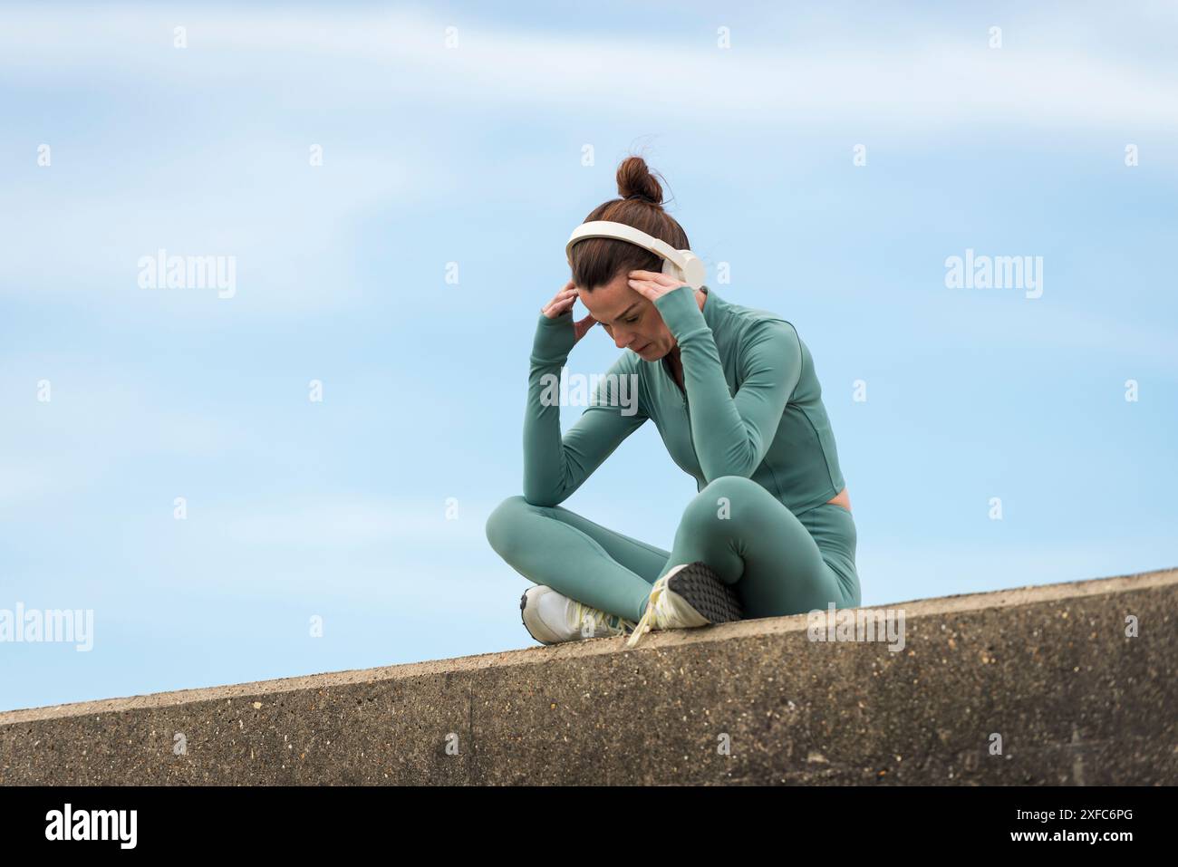 Sportliche Frau, die mit dem Kopf in den Händen sitzt und Kopfhörer trägt. Motivationskonzept. Stockfoto