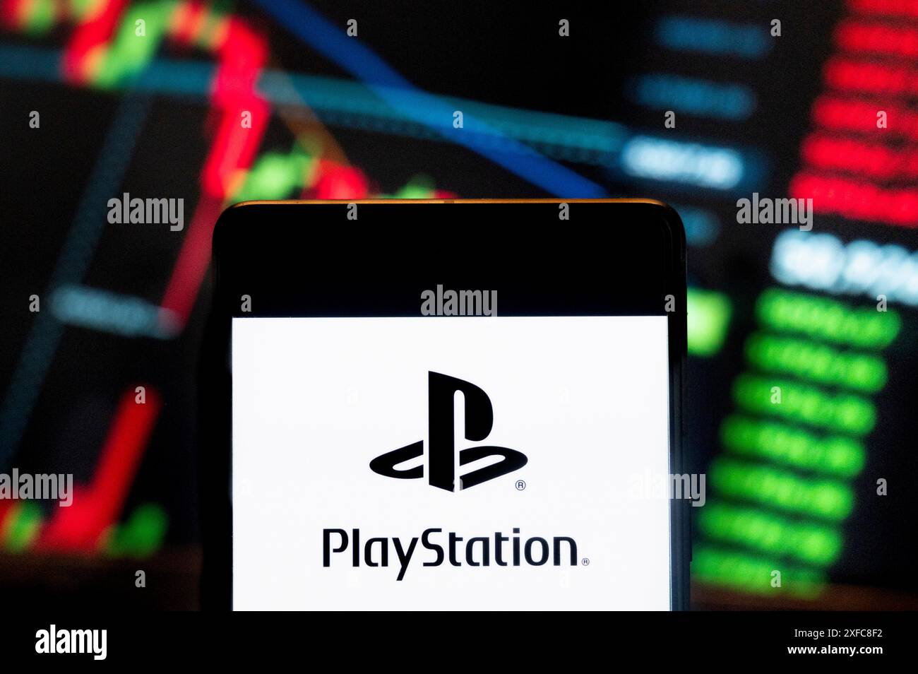 In dieser Abbildung zeigt die japanische Videospielmarke, die Sony Computer Entertainment, PlayStation (PS) gehört. Das Logo wird auf einem Smartphone mit einem Index der wirtschaftlichen Börsen im Hintergrund angezeigt. Stockfoto