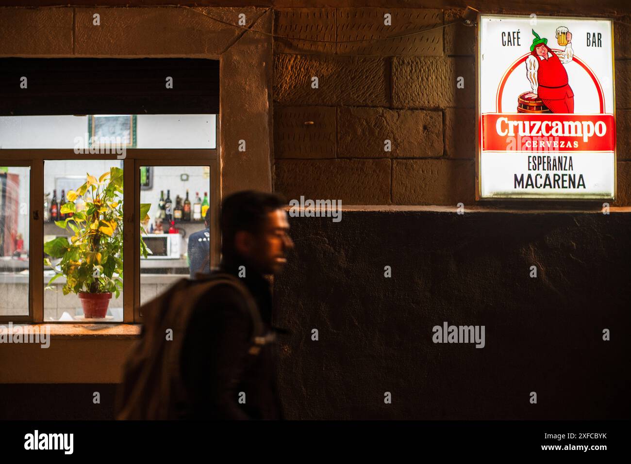 Ein Mann läuft nachts an einer typischen Bar in Sevilla, España, vorbei, wobei er sich besonders auf das leuchtende Cruzcampo-Schild konzentriert. Stockfoto Ein Mann läuft nachts an einer typischen Bar in Sevilla, España, vorbei, wobei er sich besonders auf das leuchtende Cruzcampo-Schild konzentriert. Stockfoto