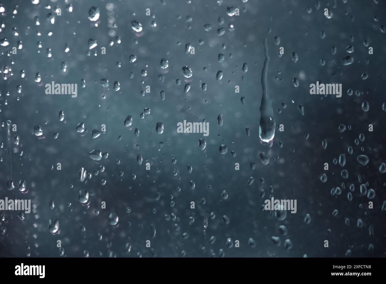 Regentropfen, die an einem dunklen, regnerischen Tag durch eine Fensterscheibe laufen, Vollformathintergrund, Konzept für deprimierendes Wetter, Kopierraum, ausgewählter Fokus Stockfoto