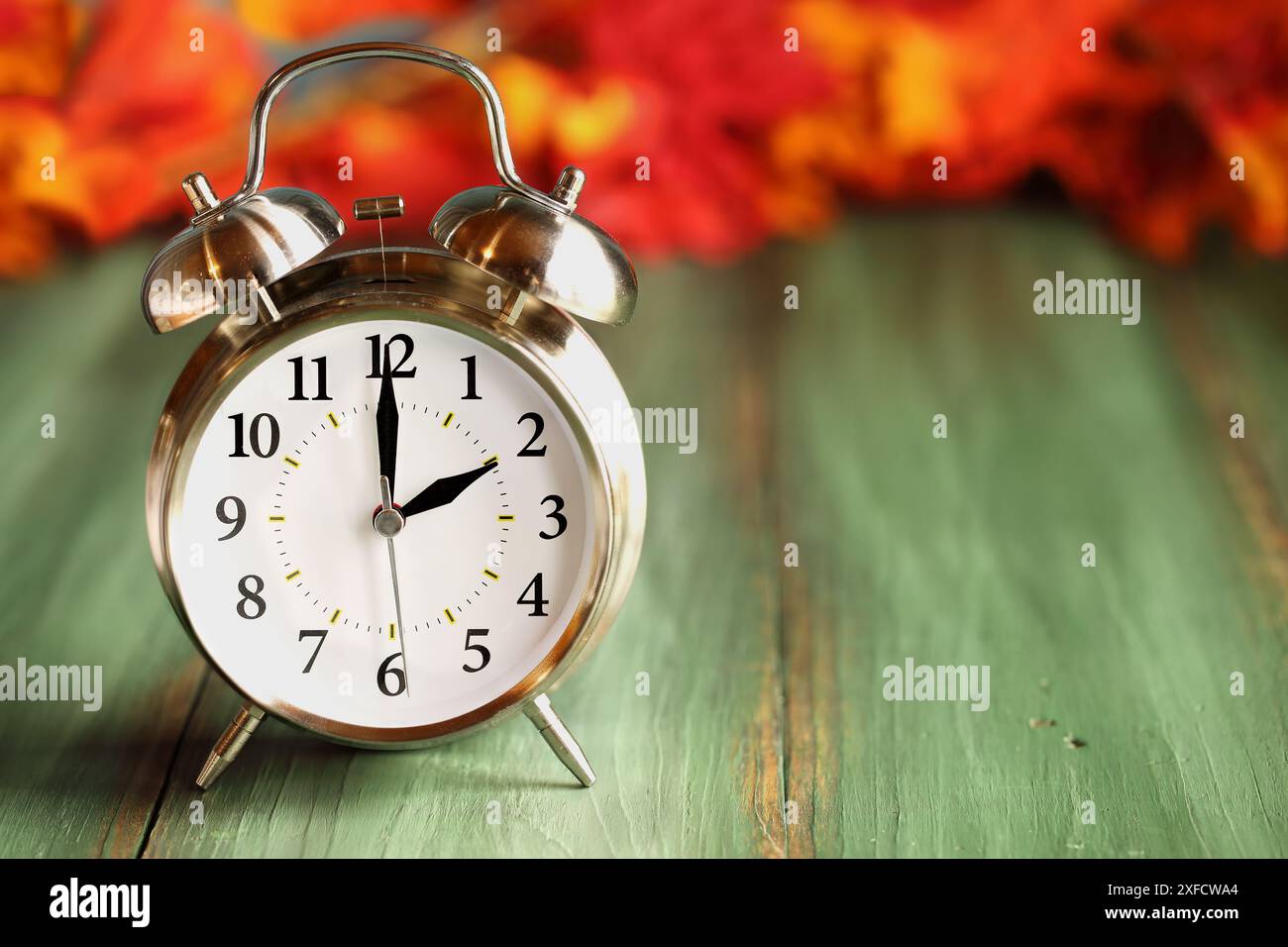 Stellen Sie Ihre Uhren zurück mit diesem Wecker mit farbenfrohen Herbstblättern über einem grünen rustikalen Holztisch. Sommerzeitkonzept. Stockfoto