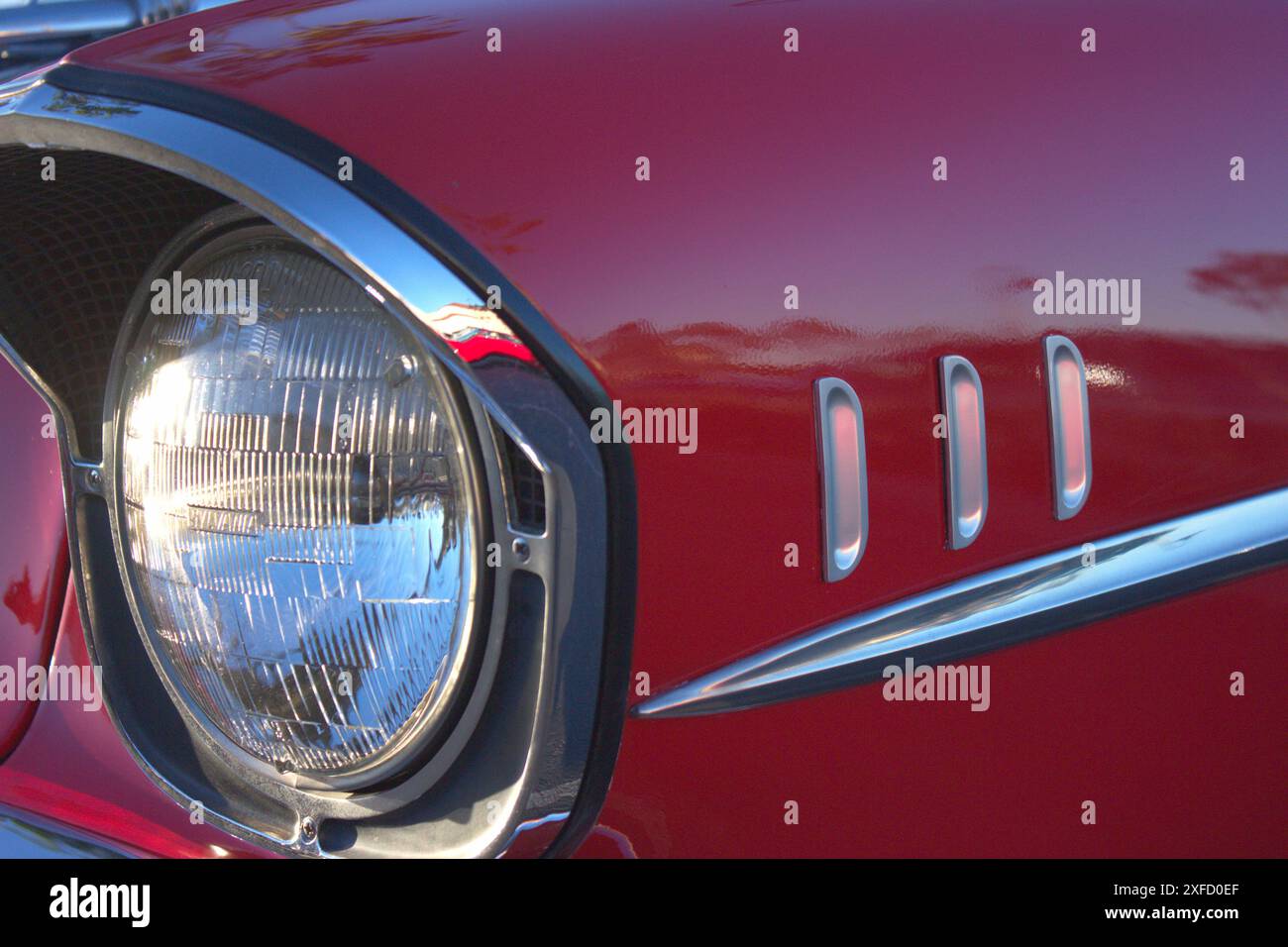 Ein detailliertes Foto des Frontscheinwerfers auf der Fahrerseite und des Kotflügels eines klassischen roten 1957 Chevy Bel Air. Stockfoto
