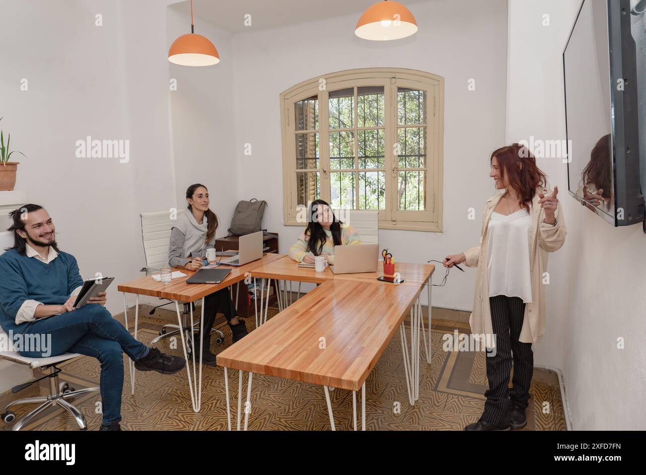 Ein Team aus verschiedenen Fachleuten nimmt an einer Präsentation in einer modernen Büroumgebung mit Laptops und einem großen Bildschirm Teil. Stockfoto
