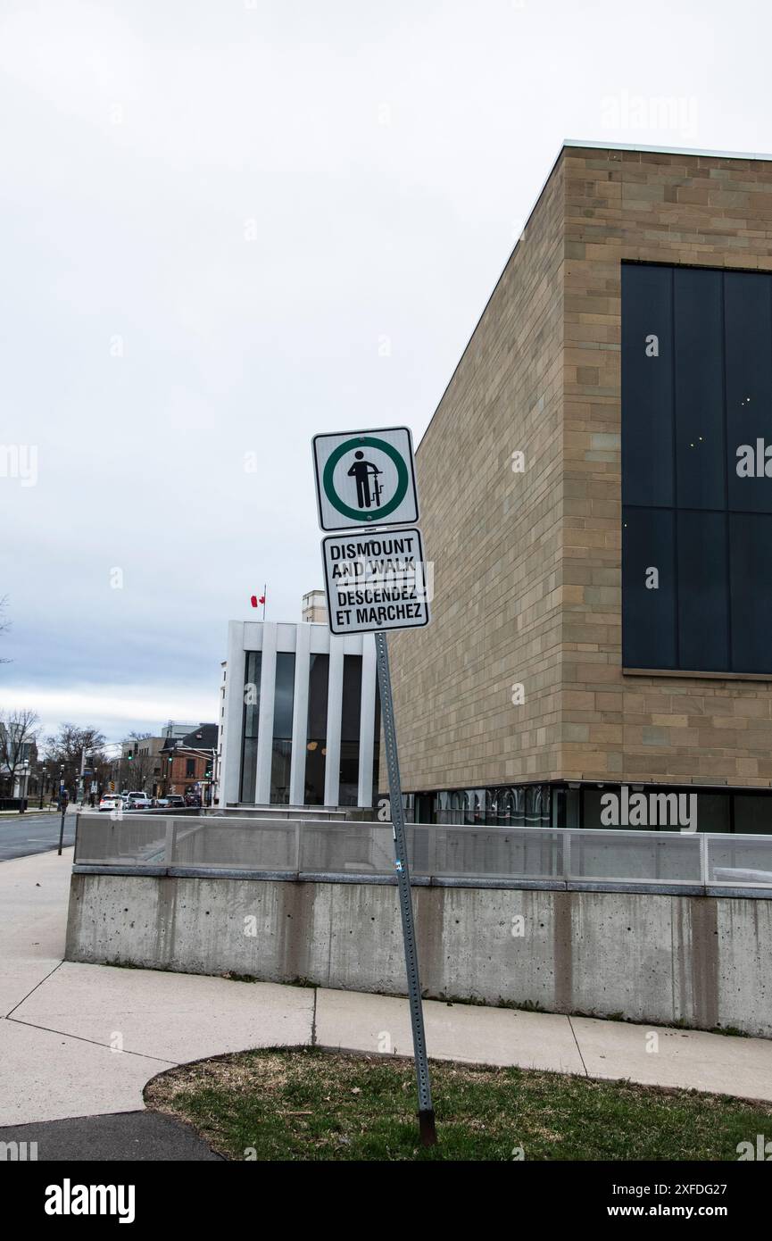 Radfahrer steigen in der Beaverbrook Art Gallery in der Queen Street in der Innenstadt von Fredericton, New Brunswick, Kanada, ab und gehen ein Schild Stockfoto