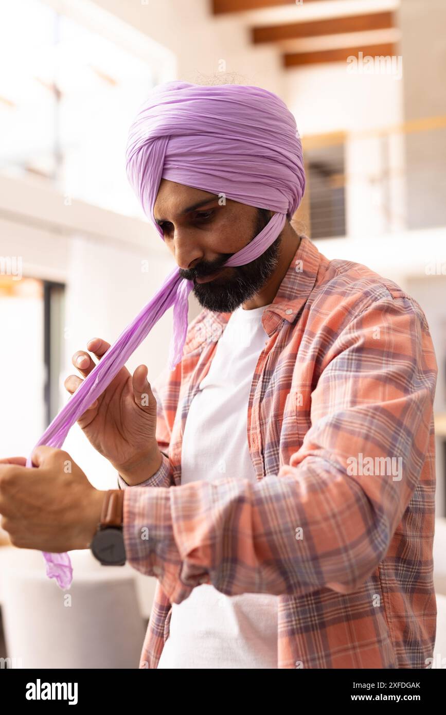 Mann, der zu Hause Purpurturban bindet und sich auf traditionelle Kleidung konzentriert Stockfoto