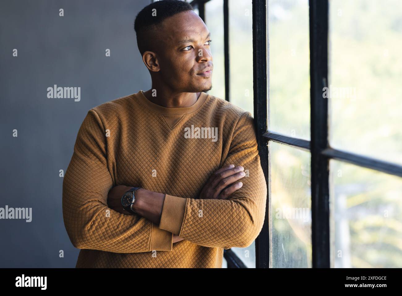 Aus dem Fenster schauend, Mann in lässigem Pullover, besinnend, Arme überkreuzt Stockfoto