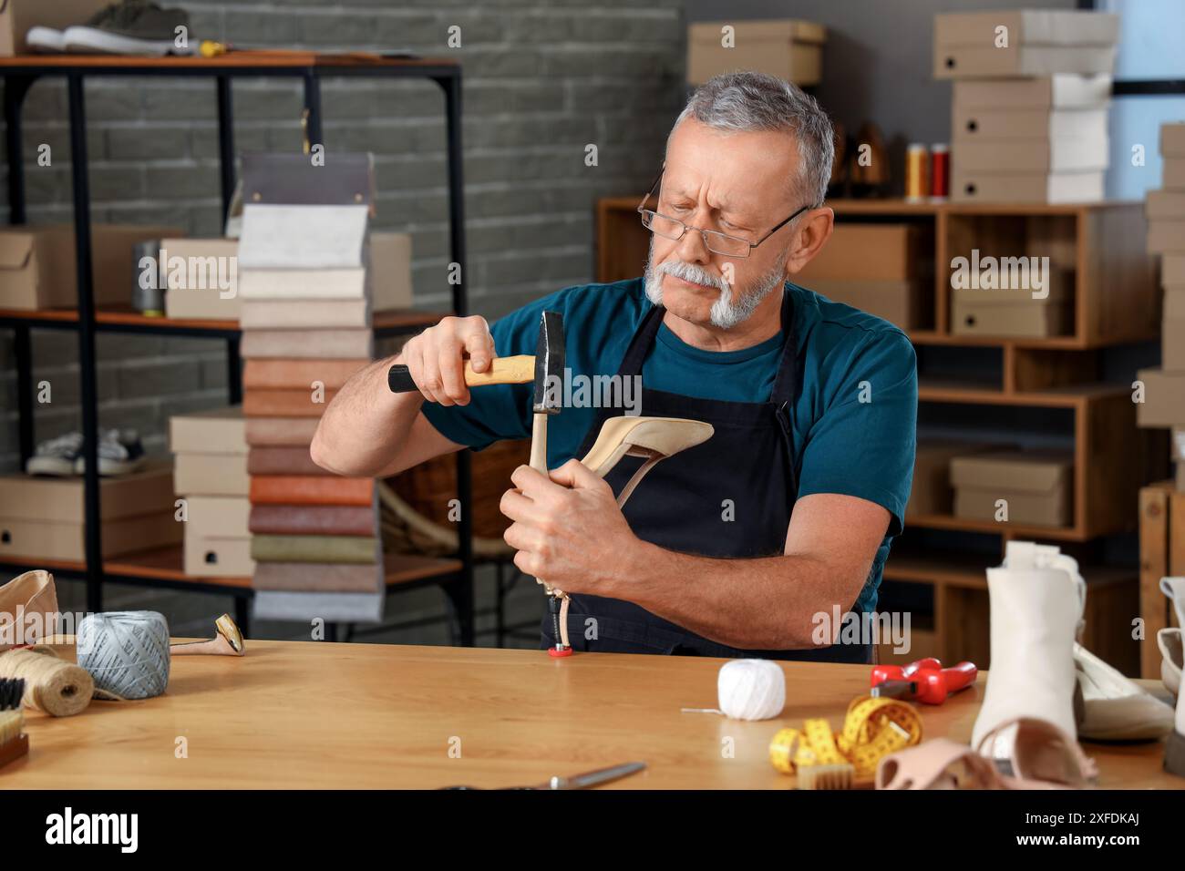 Reifer Schuhmacher repariert gebrochene Ferse am Tisch in der Werkstatt Stockfoto