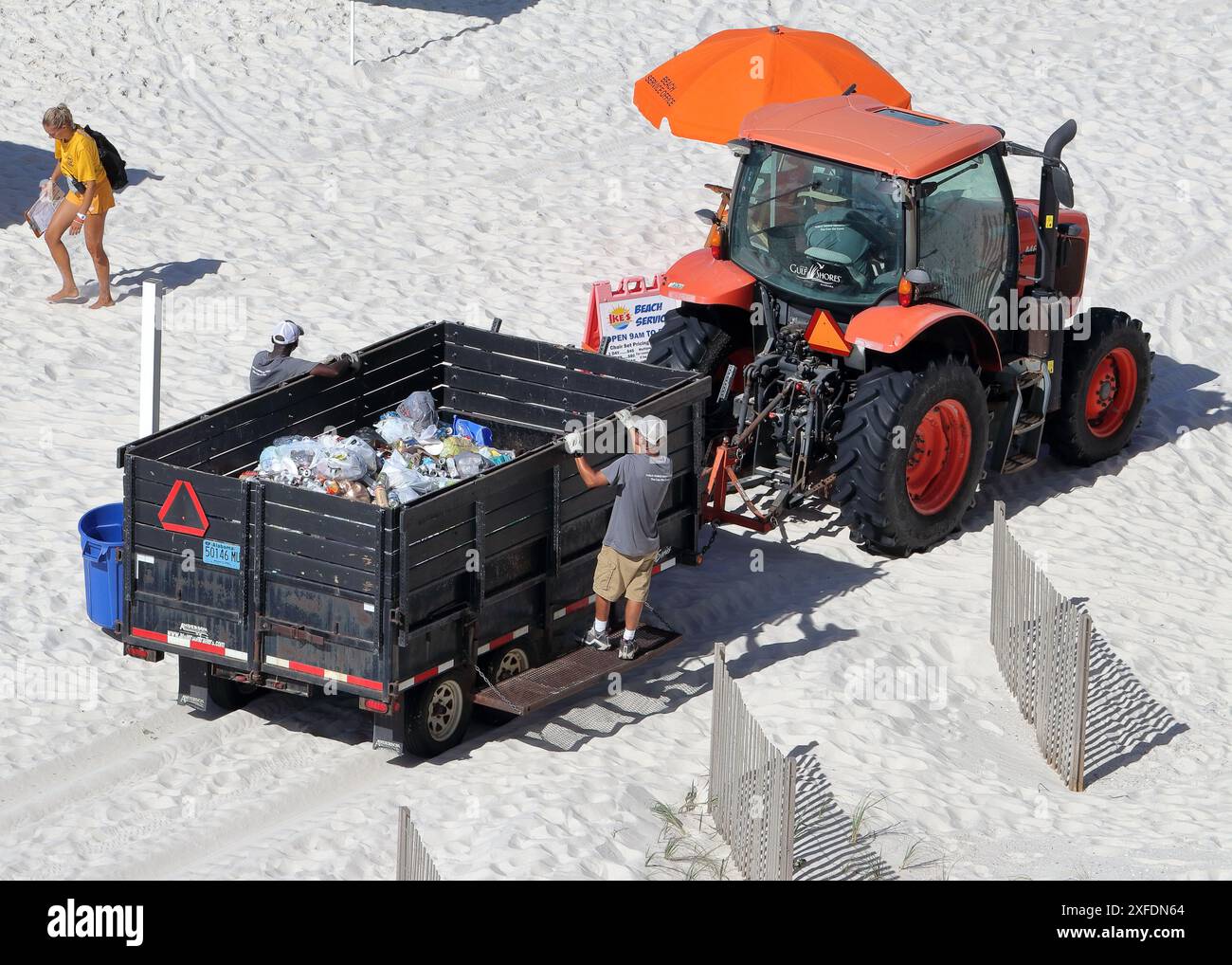 Stadtarbeiter werfen Müll aus Dosen in einen Anhänger, der von einem Traktor an einem Sandstrand gezogen wird Stockfoto