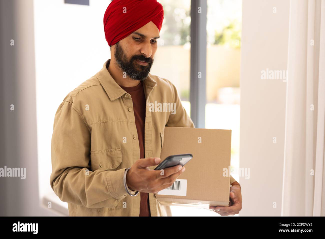 Paket halten, Mann scannt Barcode mit Smartphone zu Hause Stockfoto