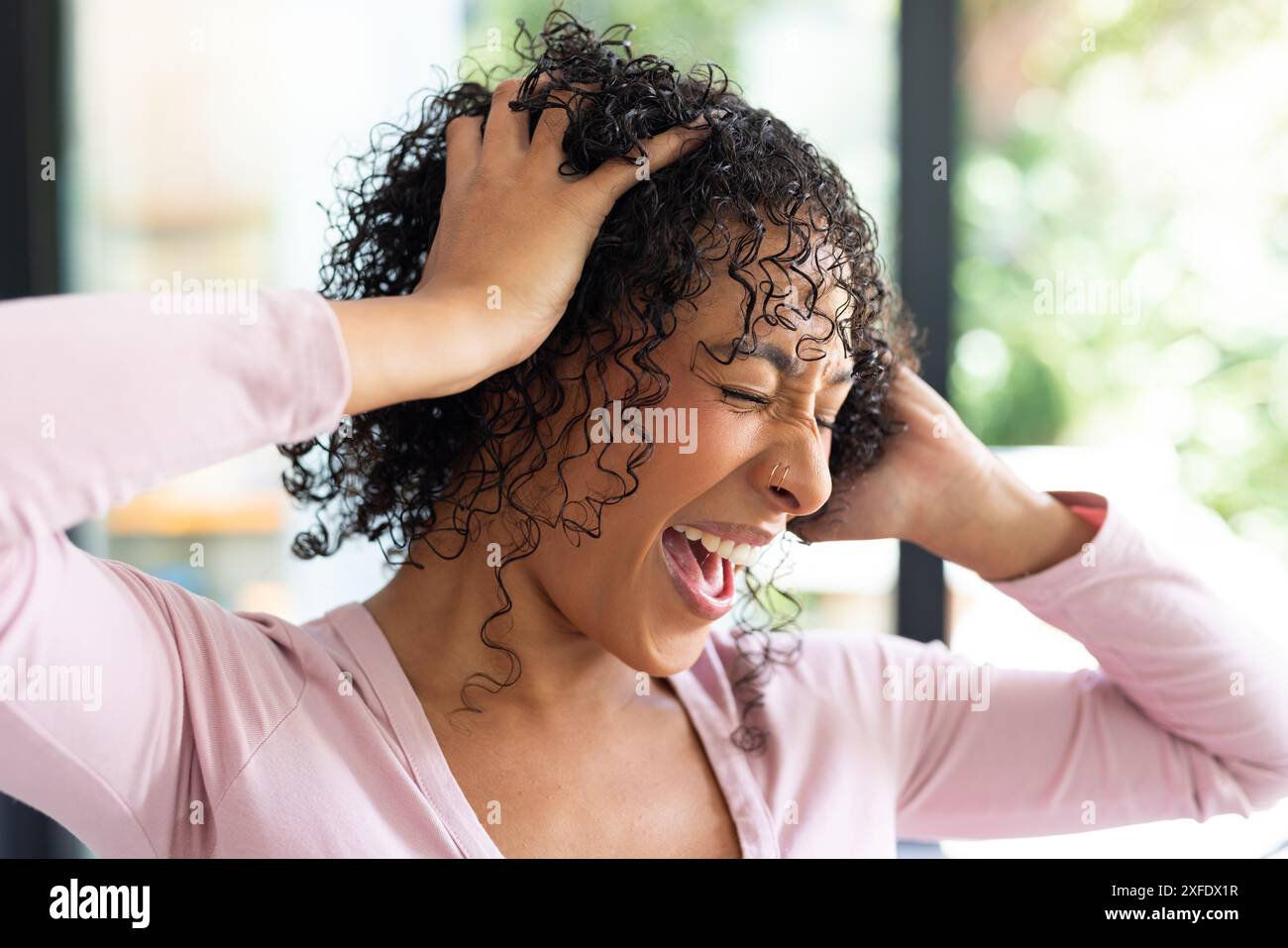 Frustrierte Frau, die den Kopf mit den Händen hält und in der häuslichen Umgebung schreiend Stockfoto