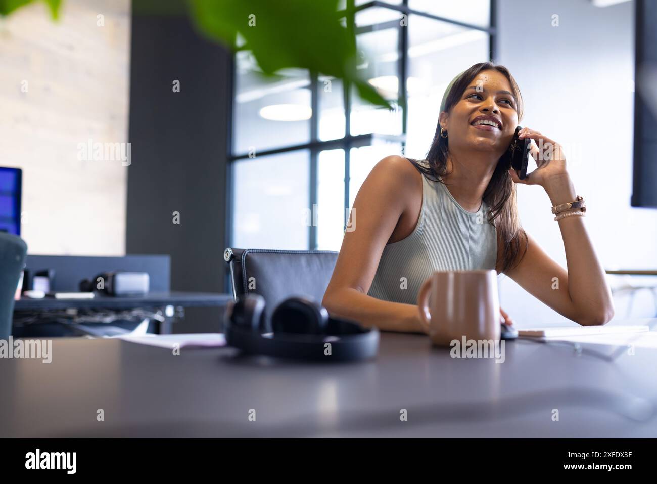 Telefonierte am Telefon, Frau sitzt am Schreibtisch mit Kaffeetasse im modernen Büro Stockfoto