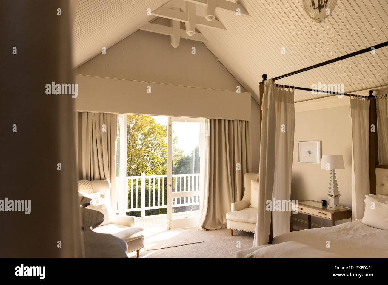 Helles Schlafzimmer mit Himmelbett und gemütlichem Sitzbereich in der Nähe eines großen Fensters, Kopierbereich Stockfoto