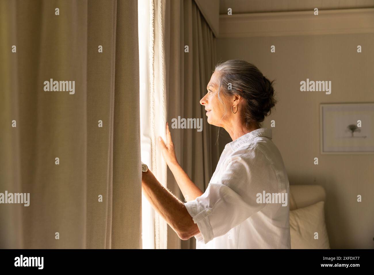 Mit Blick aus dem Fenster, reife Frau in weißem Hemd, die friedliche Momente zu Hause genießt, Kopierraum Stockfoto