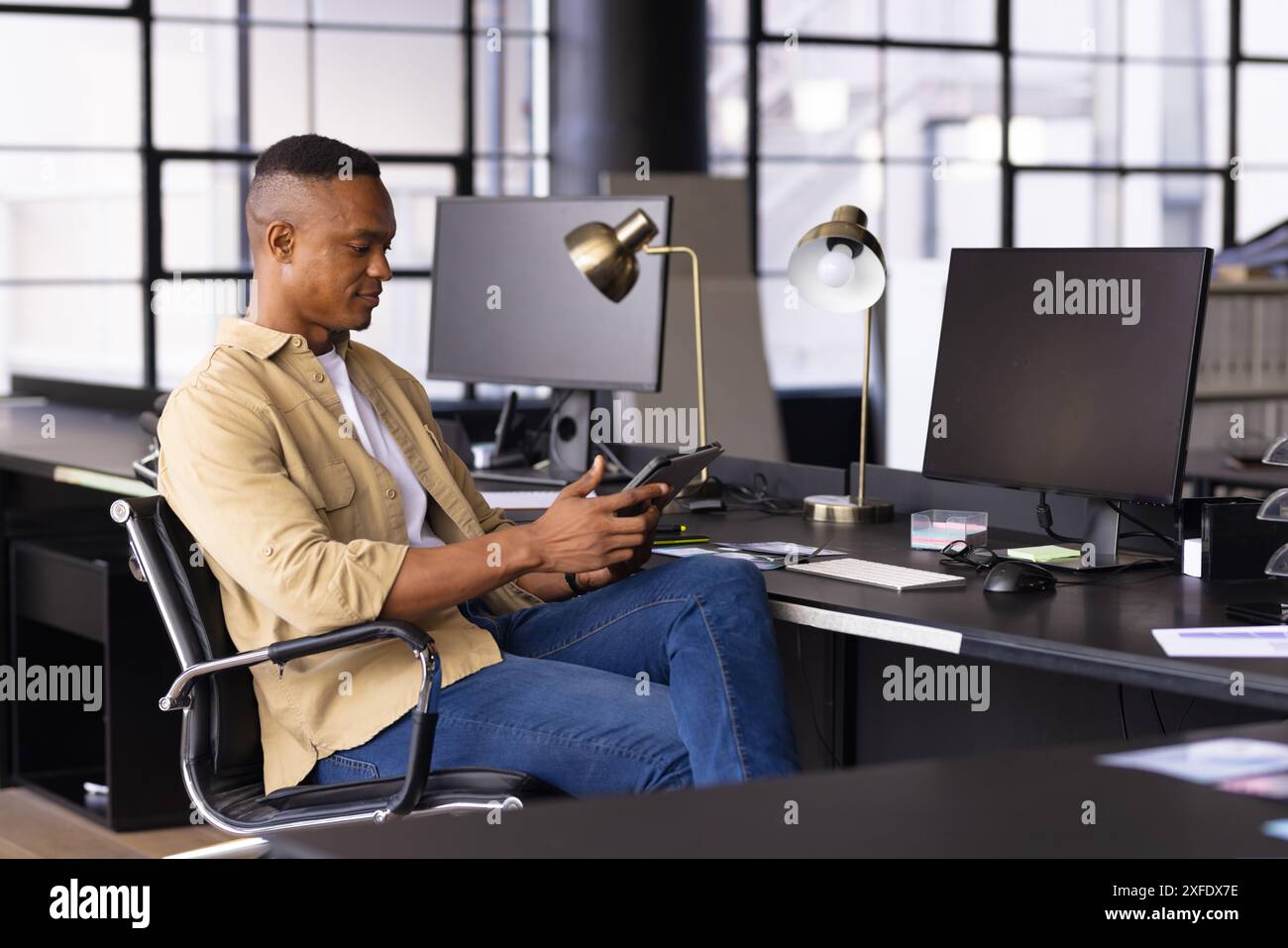 Mit einem Tablet sitzt ein Mann am Schreibtisch in einem modernen Büro und arbeitet effizient Stockfoto