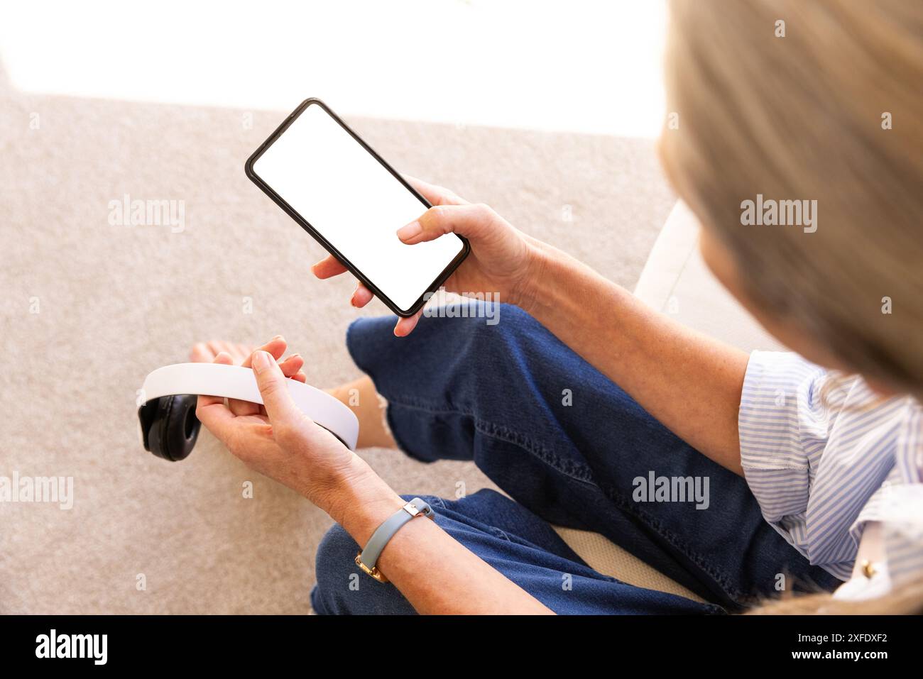 Smartphone und Kopfhörer halten, Frau, die sich zu Hause in lässiger Kleidung entspannt Stockfoto