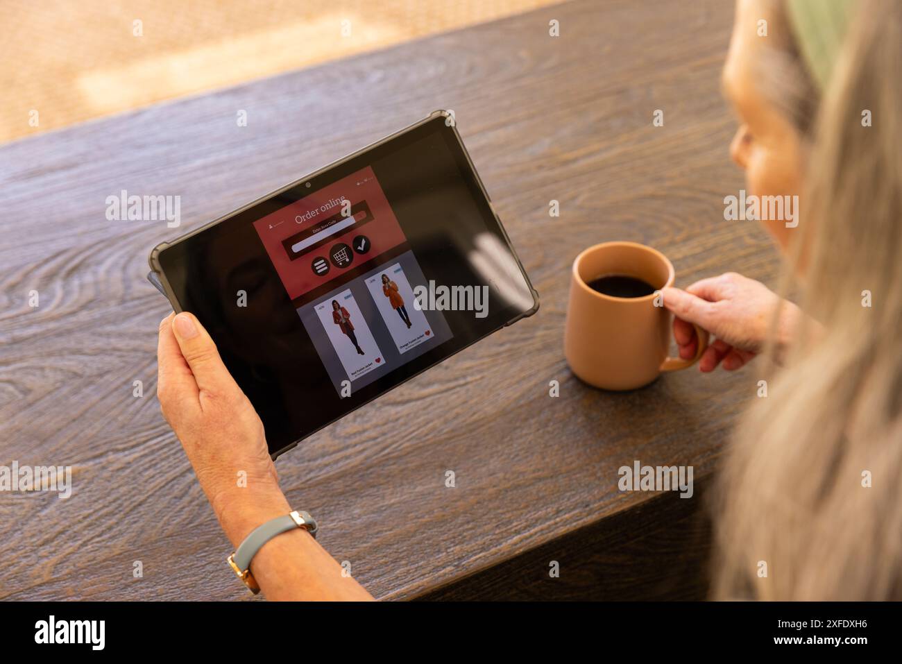 Auf dem Tablet durchstöbern, reife Frau hält zu Hause eine Kaffeetasse Stockfoto