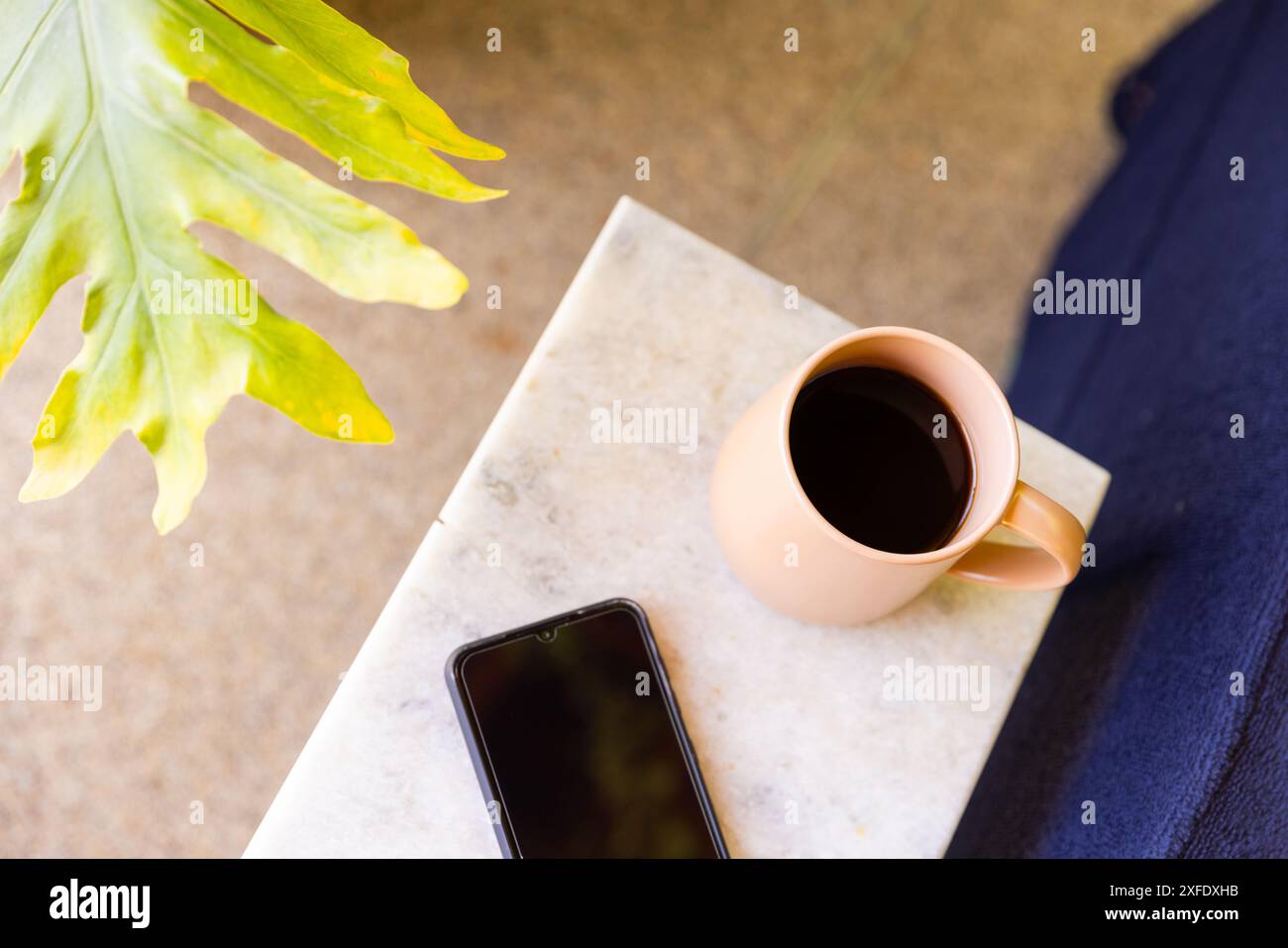 Kaffeetasse und Smartphone auf dem Tisch neben grünem Pflanzenblatt, Kopierraum Stockfoto