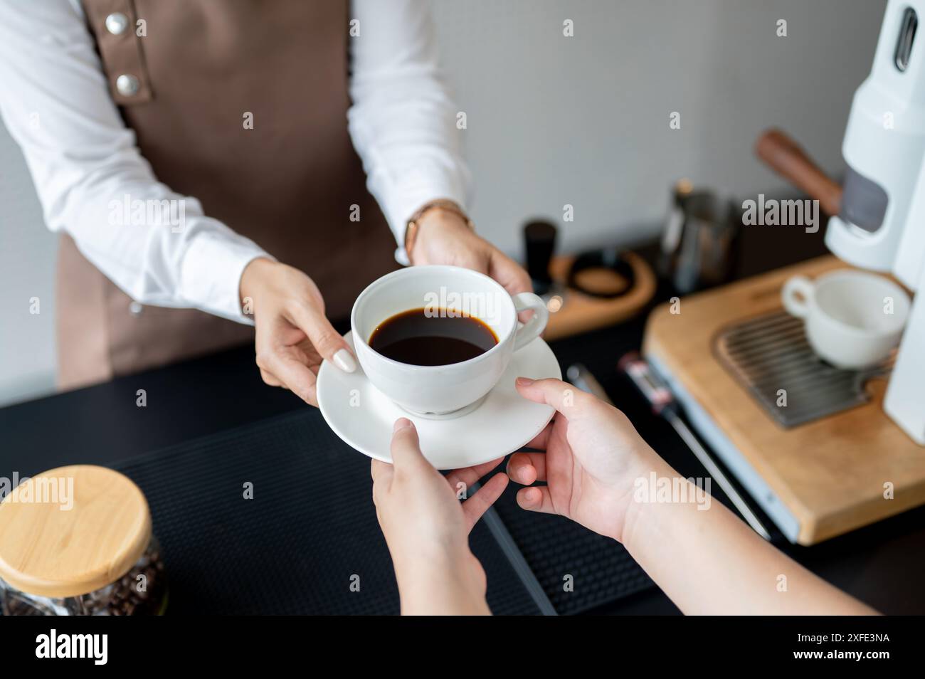 Ein Nahaufnahme eines weiblichen Barista, der einer Kundin eine Kaffeetasse über eine Theke gibt, die in einem Café arbeitet. Service, Kleinunternehmen, Teilzeit j Stockfoto