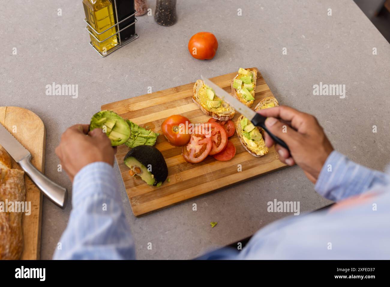 Zubereitung von Avocado und Tomaten Toast, Mann schneidet Gemüse auf hölzernem Schneidebrett Stockfoto